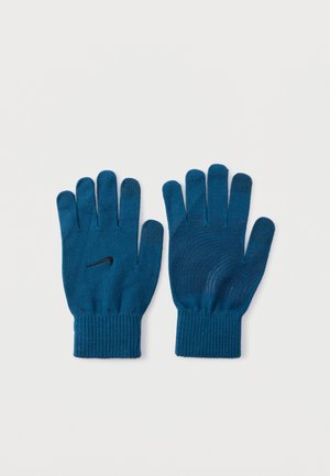 Par de guantes de punto azules con el logo negro de Nike en la parte posterior y líneas de agarre en la palma y los dedos, colocados planos sobre una superficie blanca.