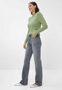 Maglietta verde a righe con maniche lunghe, jeans grigi a gamba dritta e scarpe argentate a punta. Texture lisce e design aderente.