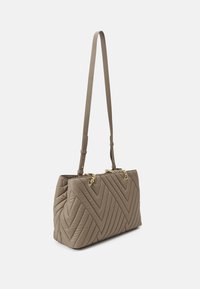 Sac à main taupe matelassé avec des coutures en chevron, des accents en chaîne dorée et une longue bandoulière réglable sur un fond blanc.