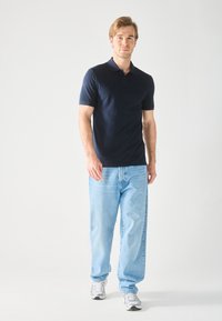 Polo shirt marine à manches courtes, associé à un jean léger bleu clair ample et des chaussures de sport argentées. Design simple et décontracté.