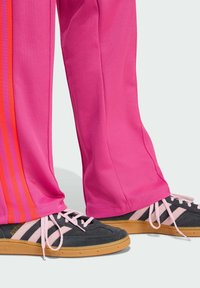 Roze sportbroek met oranje strepen aan de zijkanten, gecombineerd met zwart-roze sneakers met een rubberen zool en vetersluiting.
