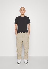 T-shirt nera in cotone, pantaloni cargo beige in nylon con tasche e sneakers bianche con un accento nero sulla suola. Tessuto liscio e vestibilità rilassata.