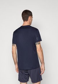 Marinblå idrottströja med korta ärmar, slät textur och diskret branding på ärmen; bärs med matchande shorts.