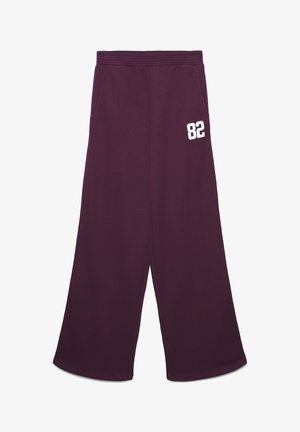 Fioletowe spodnie dresowe z szerokimi nogawkami, elastycznym pasem, bocznymi kieszeniami i białym napisem "82" na górnej części uda.