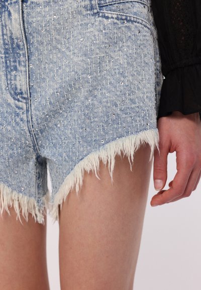 Denim kratke hlače s razrahljanimi robovi, svetlo modre barve, z razpršenimi srebrnimi okrasnimi detajli. Povečan pogled na teksturo tkanine.