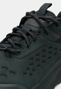 Czarne sportowe buty z teksturowanym cholewką, zaokrąglonym noskiem i skomplikowanym systemem sznurowania. Logo na języku, wzmocniona pięta i przewiewny design.