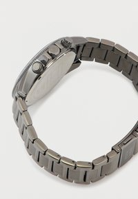 Orologio in metallo argentato con cassa rotonda, lunetta testurizzata e due pulsanti laterali. Dotato di un bracciale a maglie con finitura lucida e una fibbia.