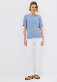 Světle modrý krátký rukávový top s texturovaným vzorem, v kombinaci s bílými rovnými kalhotami a hnědými sandály s pletenými detaily.