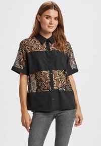 Zwarte blouse met knopen, voorzien van doorschijnende kantpanelen met bloemenpatronen. Korte mouwen en een kraag met een stevige onderkant.