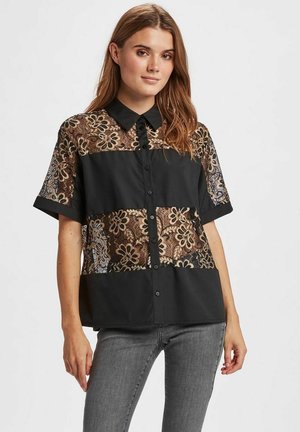 Zwarte blouse met knopen, voorzien van doorschijnende kantpanelen met bloemenpatronen. Korte mouwen en een kraag met een stevige onderkant.