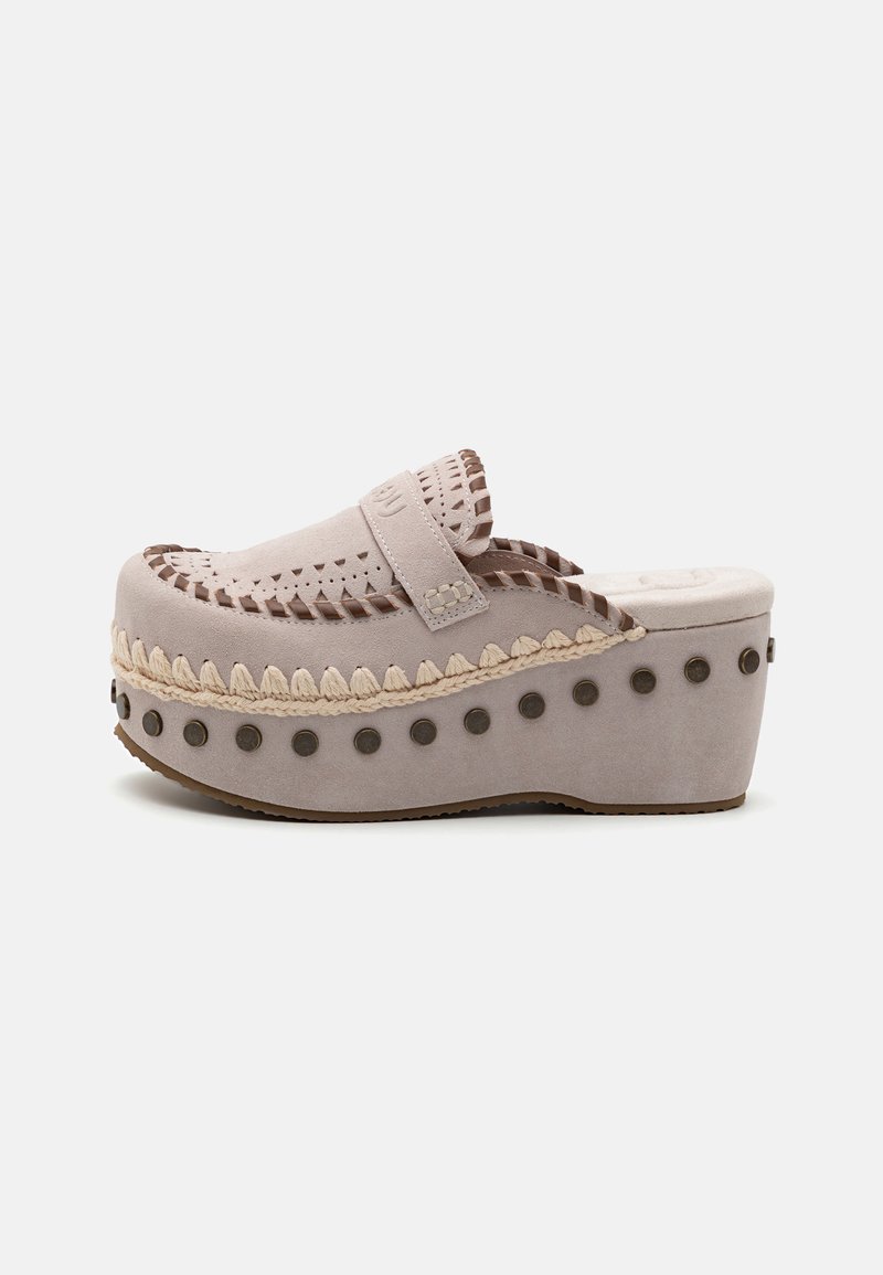 Sabot plateforme beige clair avec un dessus en suede texturé, des détails en tresses et des clous décoratifs le long de la semelle intermédiaire. Design à bout fermé.