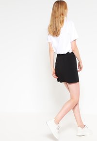 Svart kjol med midja som sitter tajt och rak skärning, i kombination med en enkel vit t-shirt och vita sneakers, sedd bakifrån.