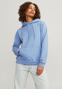 Light blue hoodie with adjustable drawstrings, front pouch pocket, and ribbed cuffs, paired with light jeans. Casual design, soft fabric.