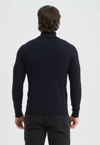 Pull col roulé marine en maille, avec des manches longues et une coupe ajustée, porté avec un pantalon foncé.