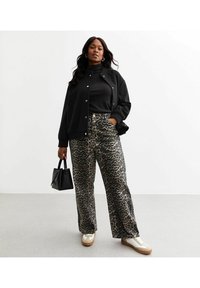 Schwarze Bomberjacke, schwarzes Shirt, weite Leopardenmusterhose, goldene Akzente, cremefarbene Sneaker mit braunen Sohlen und eine kleine schwarze Handtasche.