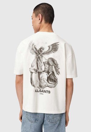 Mann trägt weißes T-Shirt mit schwarz-weißem Motiv von zwei Engeln, einer steht mit ausgebreiteten Flügeln und einer kniet an einem Grabstein, Text "ALLSAINTS LONDON".
