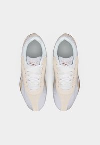 Ζευγάρι μπεζ και λευκά αθλητικά παπούτσια Reebok με λευκά κορδόνια, σε θέαση από πάνω σε απλό ανοιχτό φόντο.