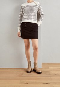 Maglione lavorato a maglia color crema con motivo geometrico grigio, mini gonna nera con dettaglio a doppio bottone e stivali alla caviglia color beige con suole nere.