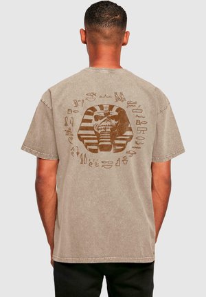 Braunes Baumwoll-T-Shirt mit lockerer Passform. Auf der Rückseite befindet sich ein Grafik eines Pharaonenhauptes, umgeben von Hieroglyphen. Kurzärmlig.
