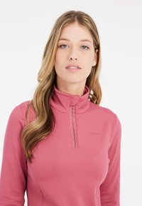 Top lungo a maniche rosa con colletto alto, caratterizzato da una chiusura a mezza zip e un sottile logo del brand sul petto. Tessuto morbido e design aderente.