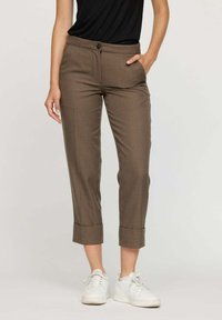 Pantalons à carreaux marron avec une coupe ajustée, ourlets à revers, deux poches avant et fermeture à bouton. Associé à des baskets blanches.