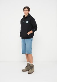 Moletom preto com bolso frontal e design gráfico, combinado com calções de ganga e botas ankle cinza claro. Apresenta um corte casual e uma textura suave.