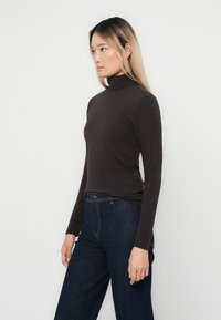 Brun långärmad tröja med hög krage i ett slätt tyg, tight passform, kombinerad med mörkblå vida jeans.