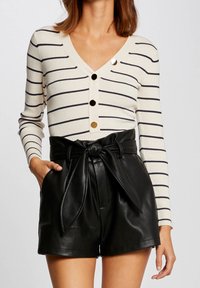 Randig krämfärgad och marinblå ribbad cardigan med V-ringning och guldknappar, tillsammans med högmidjade svarta lädershorts med knutet bälte.