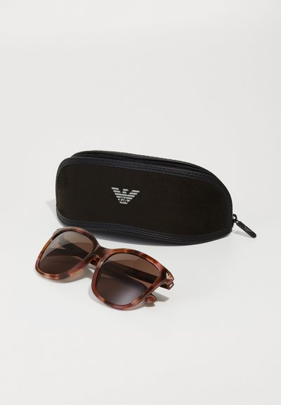 Ruskean kilpikonnakuosisunglasses tummilla linsseillä, neliömäinen muoto ja kultaiset yksityiskohdat; mukana musta vetoketjullinen kotelo, jossa on logo.