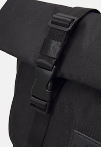 Sac messager noir avec un tissu texturé, une fermeture enroulable et une boucle en plastique robuste pour un maintien sécurisé.