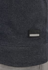 Felpa blu navy con tessuto strutturato, orlo a coste e un'etichetta rettangolare nera con strisce bianche di accento.