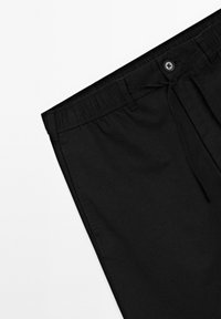 Black elastic waist pants with front button, belt loops, drawstring ties, and side pockets on a white background.