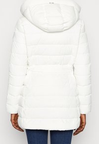 Chaqueta acolchada blanca con capucha, que presenta una cintura ceñida y un diseño acolchado. Textura suave con acabado liso y sin hardware visible.