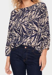 Top w kwiatowy wzór w granatowym i kremowym kolorze, z długimi rękawami i luźnym krojem, wykonany z lekkiego materiału; zestawiony z ciemnymi dżinsami.