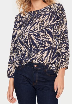 Bluse mit floralem Muster in Marineblau und Creme, mit langen Ärmeln und lockerer Passform, aus leichtem Stoff; kombiniert mit dunklen Jeans.