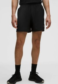 Pantalones cortos deportivos negros hechos de tela ligera, con cinturilla elástica y un detalle sutil de logo. La longitud llega a la mitad del muslo.