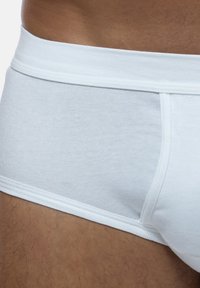 Weiße Baumwoll-Boxerbriefs mit glatter Textur, elastischem Bund und genähten Nähten, die einen Teil eines Beins mit hellem Haar zeigen.