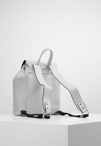 Zaino in pelle grigia con chiusura a rotolo, manici piatti e cinturini regolabili. Presenta un design minimalista e accenti neri.