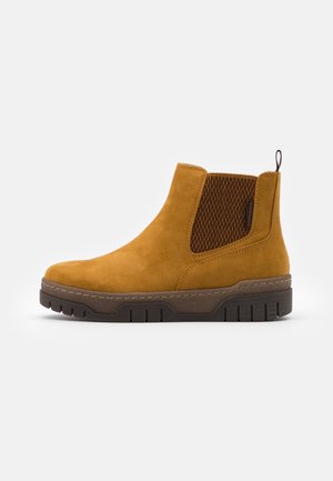 Tan ruskind Chelsea-støvle med mørkebrun elastisk sidepanel og tyk tekstureret sål, velegnet til afslappet brug.