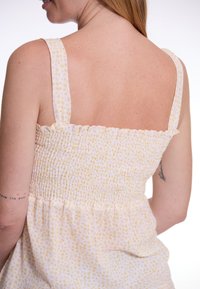 Weißes Kleid mit gelbem Blumenmuster. Verfügt über einen gerafften Oberteil und breite Schulterträger. Leichter, texturierter Stoff und ausgestellte Silhouette.