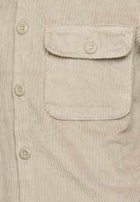 Beige fløjls-skjorte med lodrette striber. Har knaplukning og brystlomme. Blød tekstur med holdbare syninger.