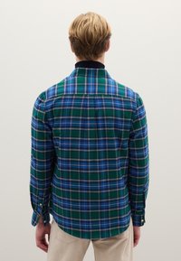 Camisa de cuadros en verde y azul con botones, cuello, mangas largas y dobladillo curvado. Hecha de tela con textura suave. Detalles de costuras blancas.