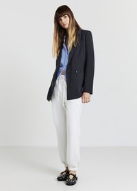 Blazer noir ajusté sur une chemise rayée bleu clair, associé à un pantalon de survêtement gris et des chaussures noires à enfiler avec des œillets.