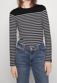 Chemise à manches longues noir et blanc à rayures avec un col rond, associée à un jean en denim bleu taille haute avec une fermeture à bouton à l'avant.