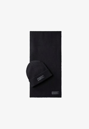 Zwart geribd gebreide muts en bijpassende sjaal met Calvin Klein logo-patches op een witte achtergrond.