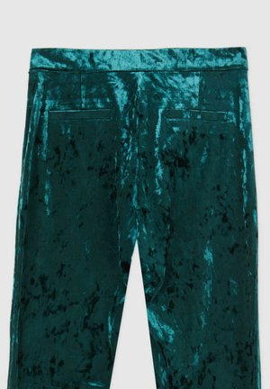Pantaloni verdi in velluto con una texture morbida, dotati di due tasche posteriori e di una cintura liscia, che mostrano una leggera lucentezza e un motivo uniforme.