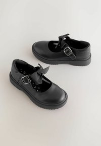 Zwarte leren Mary Jane schoenen met een afgeronde neus, verstelbare gespsluiting en een decoratieve strik aan de voorkant. Textuurzool met sterren.