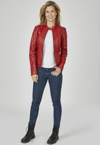 Rote Lederjacke mit tailliertem Design, hohem Kragen und frontalem Reißverschluss. Kombiniert mit einem weißen T-Shirt, dunkelblauen Jeans und schwarzen Schnürstiefeln.