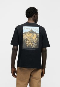 Μαύρο βαμβακερό T-shirt με κοντά μανίκια, με πολύχρωμη γραφική εκτύπωση στην πλάτη που απεικονίζει τη χλωρίδα και τους βράχους της κοιλάδας Yosemite.