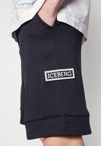 Granatowe bawełniane szorty z kieszeniami bocznymi oraz białą prostokątną naszywką z napisem "ICEBERG" w czerni. Gładka faktura i klasyczny krój.